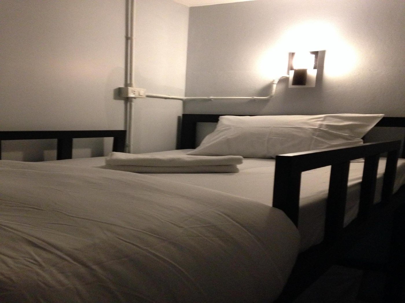 A dormitory bunk with white bedding and a wall-mounted reading light at The Metallic Hostel